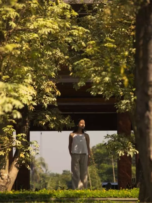 A woman is standing in front of the lobby area amidst the trees