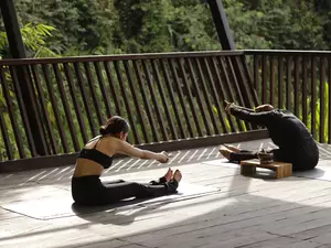 A woman is having yoga session with an instructor at the riverside deck